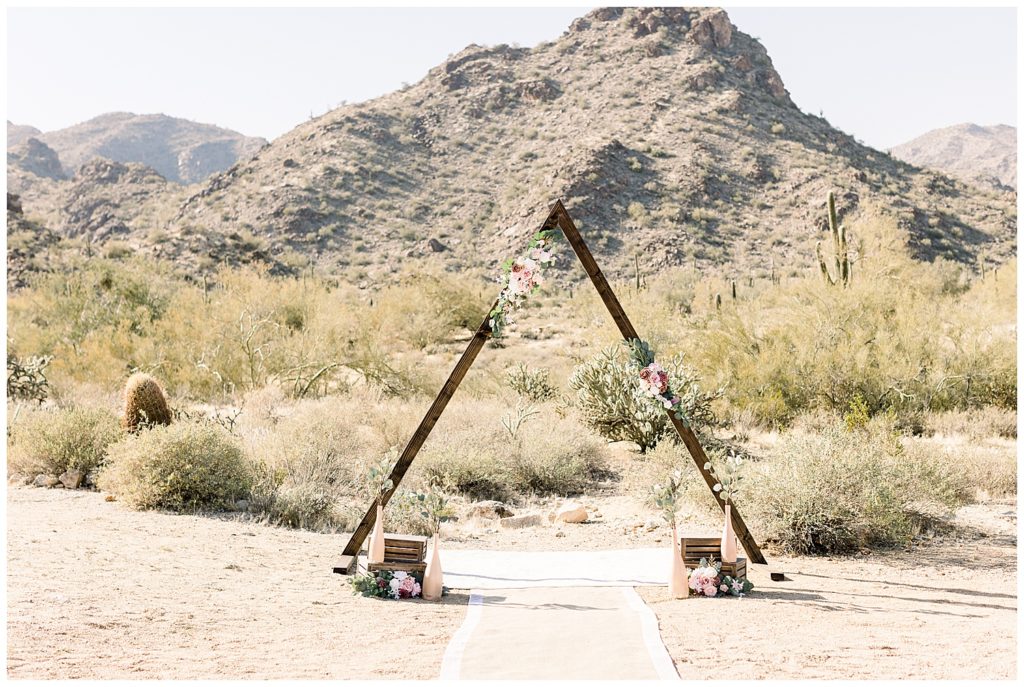 Desert Elopement in Arizona , floral triangle arch set up, boho rug and runner